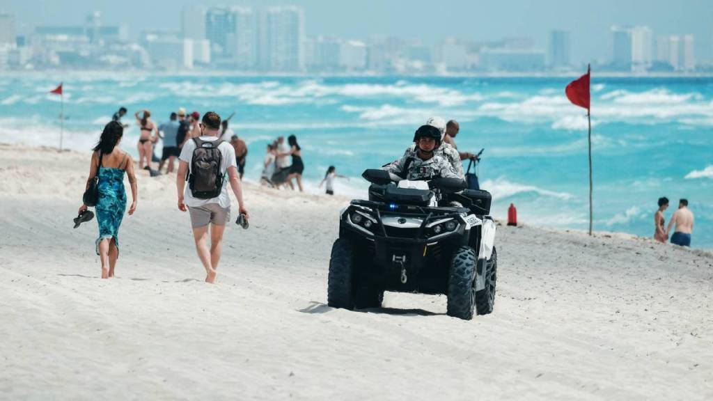 Turistas caminan en una playa de Quintana Roo, custodiados por elementos de Seguridad Ciudadana.