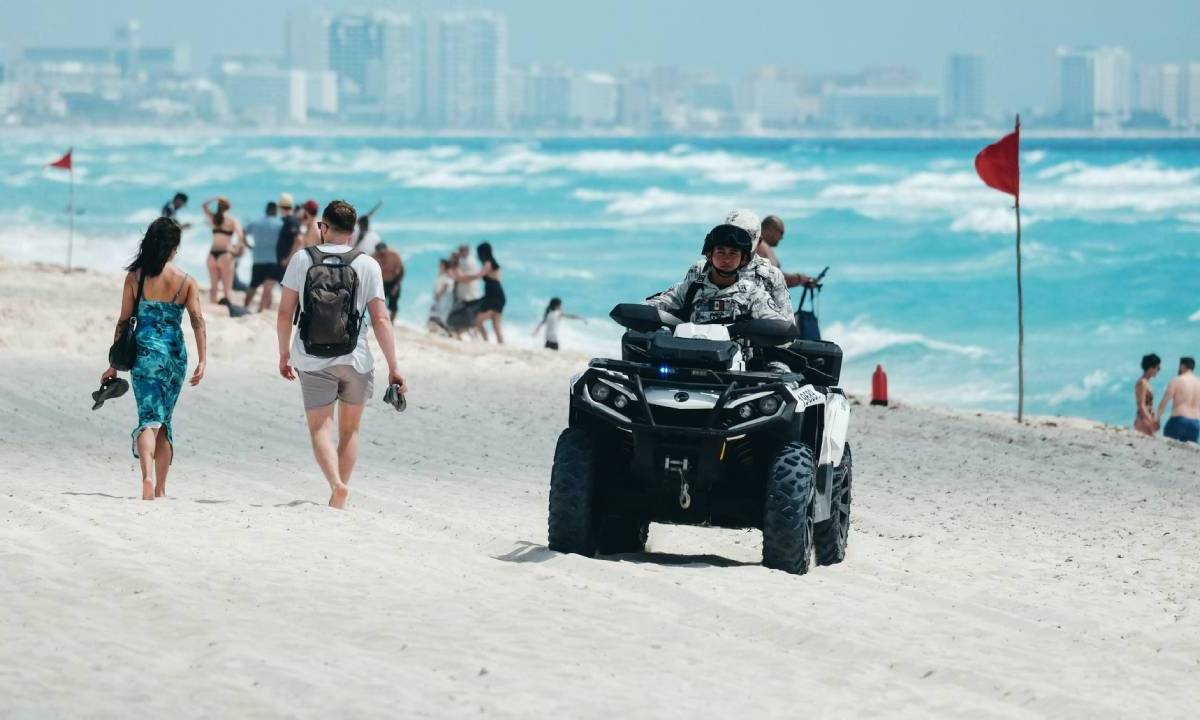 Turistas caminan en una playa de Quintana Roo, custodiados por elementos de Seguridad Ciudadana.