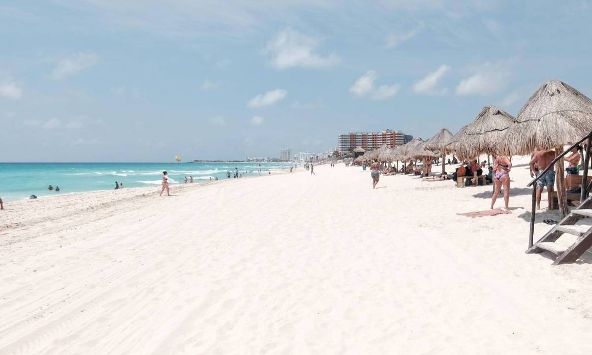 Turistas disfrutan del calor, la arena y el mar en una playa de Cancún.