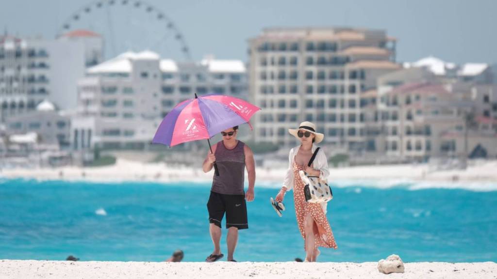 Turistas se protegen del sol mientras pasean en una playa de Cancún.