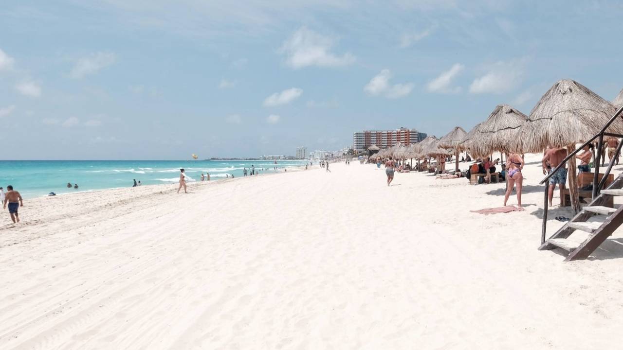Turistas disfrutan del calor, la arena y el mar en una playa de Cancún.